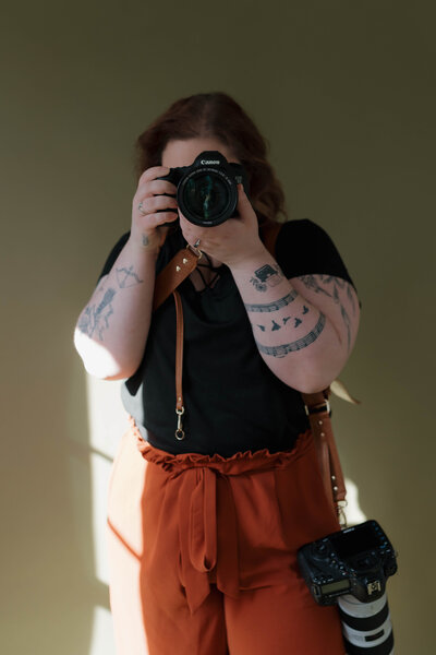 tattooed photographer holding a camera to her face