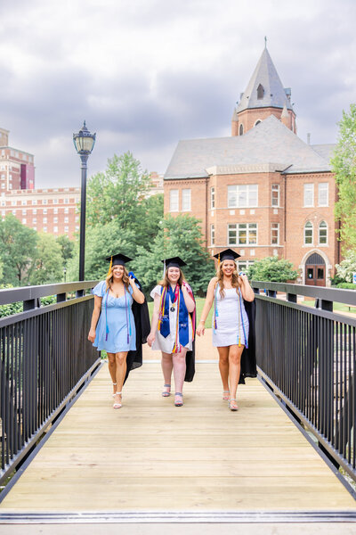 3 SLU seniors on the bridge with cap and gown in front of cupples house