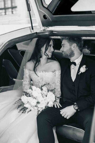 black white bride and groom sit in the back of limo in captured by Northern VA photographer in old. town Alexandria