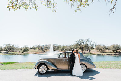 car with bride and groom kissing in front of it