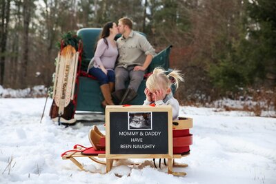 Photo of Big Sister with baby annoucement sign with parents in background