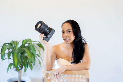 Dallas portrait photographer dressed in an elegant white outfit, holding her professional camera, showcasing expertise and style as a top Dallas photographer in Dallas, TX