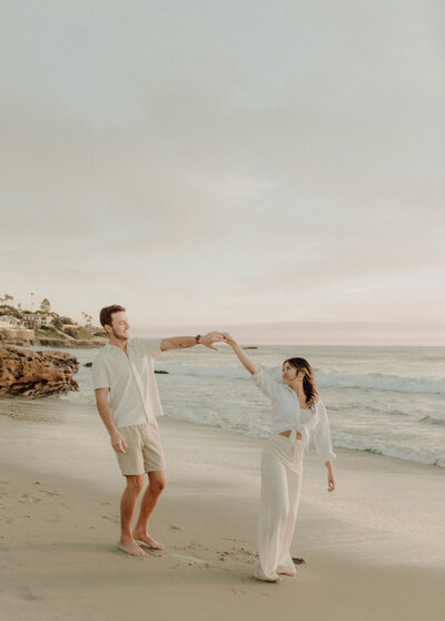 couple holding hands and twirling in front of beach