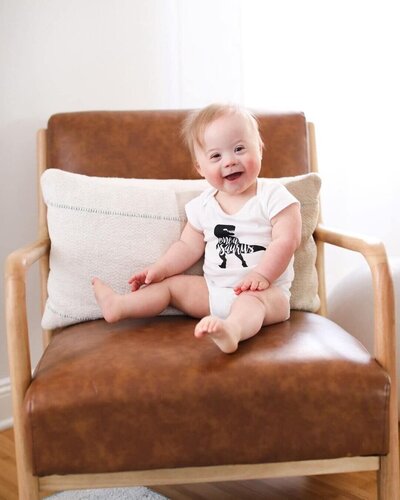 Image shows a baby smiling and sitting on a leather chair