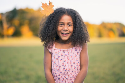 Girl smiling with a leaf on her head, photographed by Boston family photographer Corey Flint.