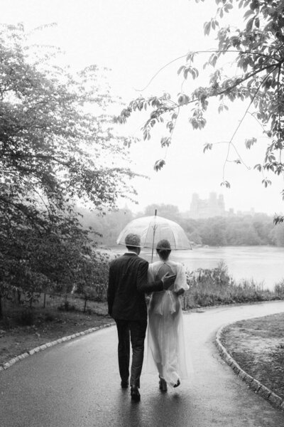 NYC central park elopement couple black and white portrait walking in the rain with umbrella surrounded by trees