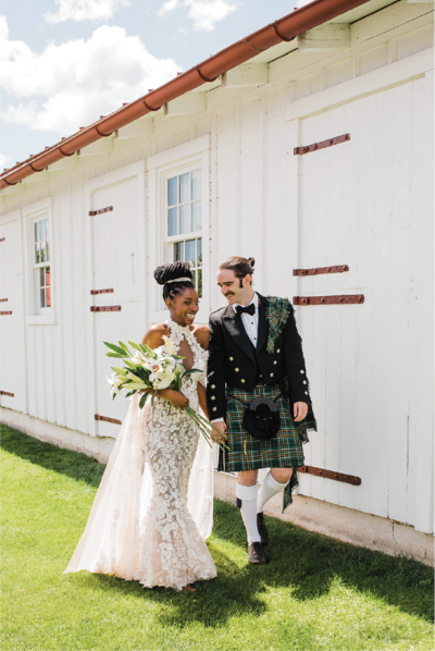 Bride and Groom in a white wedding gown and Kilt walking smiling and holding hands.