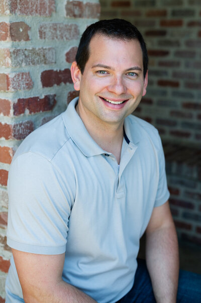 Headshot of Tim Cordell, a handsome business man in gray collared shirt sitting in front of a brick wall in San Juan Capistrano, CA