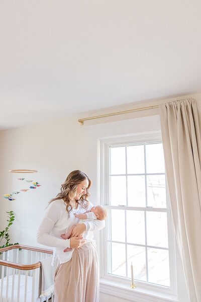 Mom stand by window with baby  during outdoor newborn photo session with Sara Sniderman Photography in Natick Massachusetts