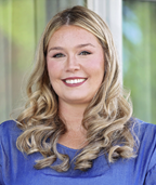 Jessica wearing a white blazer, smiling as she writes in her planner