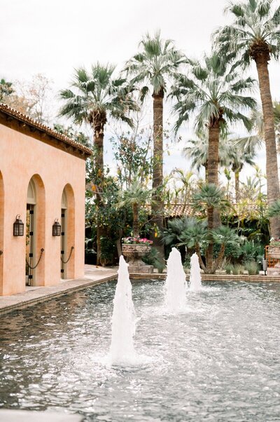 Exterior view of a luxury venue with palm trees and fountain.