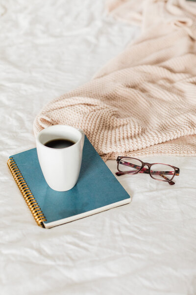 Cup of coffee and notebook on a white bed