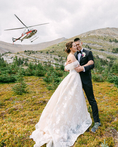 This stunning photograph captures the bride and groom holding each other during their mountain helicopter elopement. With the Alpine helicopter flying behind them, the dramatic backdrop and adventurous spirit of their wedding create an unforgettable and breathtaking moment.