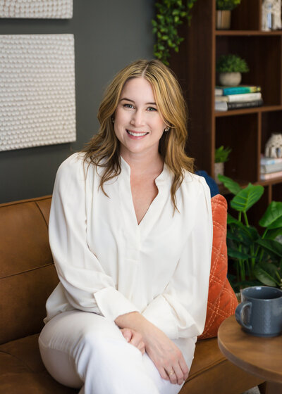 woman in a white work blazer tucking her hair behind her ear smiling
