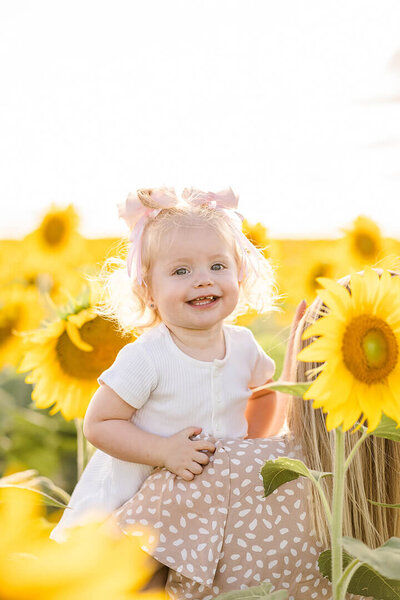 little girl on mums shoulder smiling for camera in sunflower field at brisbane