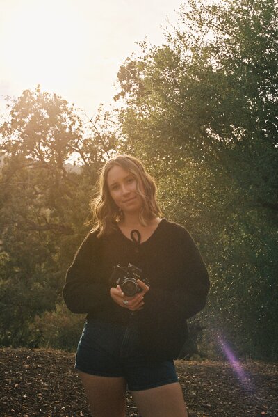 woman wearing a black hat and dress holding a camera while gently smiling