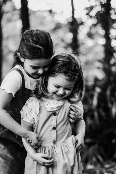Two little girls hug affectionately in a vibrant greenery setting, photographed by Bia Schaefer in Orlando, Florida.