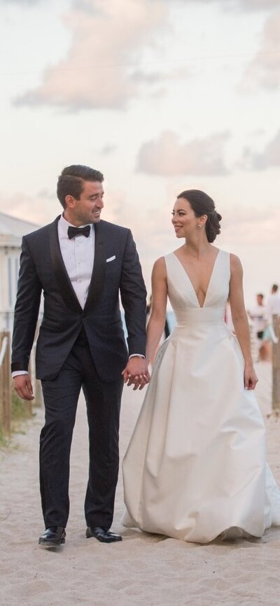 Bride and groom holding hands and walking along a beach path in Miami, Florida, captured by Rodrigo Varela Photography. Elegant and candid beach wedding photography showcasing the natural beauty and romance of a Miami wedding.