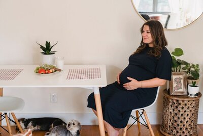 Pregnant woman sitting at a dining table holding her belly representing perinatal and postpartum therapy for body image and identity support at Rooted & Nourished Psychotherapy
