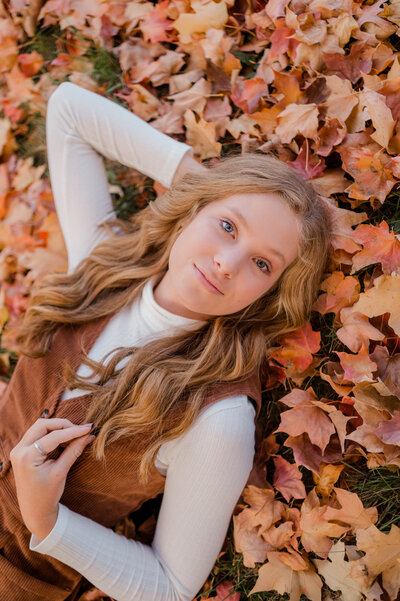 Teenage girl poses for the camera lying on autumn leaves.