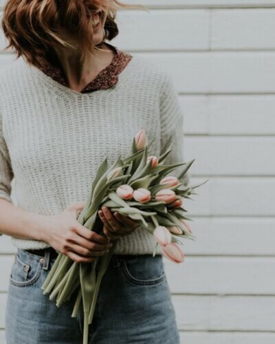 A woman joyfully presents a bouquet of tulips, featuring an array of bright colors and lush green stems.