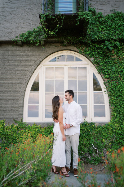 Couple posing outside in front of a wall decorated with greenery