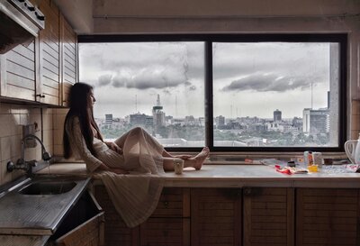 Woman in kitchen looking out of  window at the city