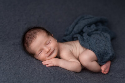 newborn boy smiling and lying on blue fabric at photo session