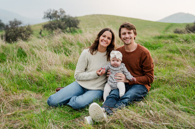Mom and dad sitting in a field with their daughter