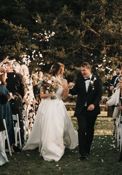 Bride and groom joyfully walking back down the aisle as guests toss petals at DuGaren Venues & Vineyards