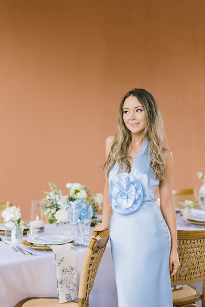 Woman in a blue dress posing beside a table