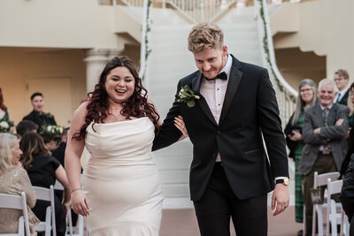 GROOM AND BRIDE HOLD HANDS AND WALK UP THE AISLE AFTER THEIR WEDDING AT ART CENTER IN CORPUS CHRISTI, TX