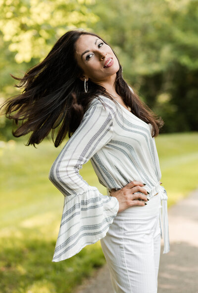Portrait of Maria K., a client of Laila's Studio, looking up with a gentle smile and her wavy, styled hair cascading over her shoulders. She appears to be wearing a light-colored, possibly striped, top.