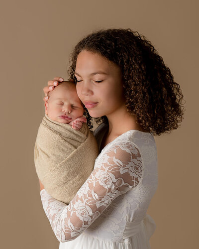Big sister holding swaddled baby.