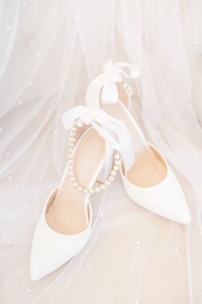 Brides white shoes with gold and white pearls sit on a stool.