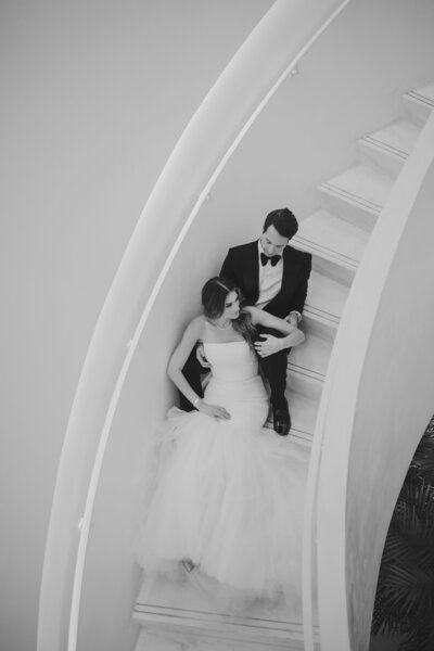 Elegant black and white portrait of a bride and groom seated on a spiral staircase, captured by Rodrigo Varela Photography in Miami, Florida. Timeless and romantic wedding photography showcasing intimate moments for couples.