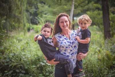 Mother in blue shirt holding two young boys wearing black shirts with hockey masks on them and holding fake plastic knives