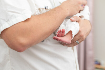 Sweet detail photo of newborn feet while dad is holding her