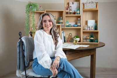 Merlyn Asencio in a white top and jeans, sitting confidently in her chair, reflecting professionalism and warmth in her trauma therapy practice in Miami, Florida