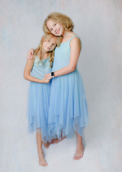 Two young girls hugging each other in matching dresses during their studio like in home family photo session in McKinney, TX.