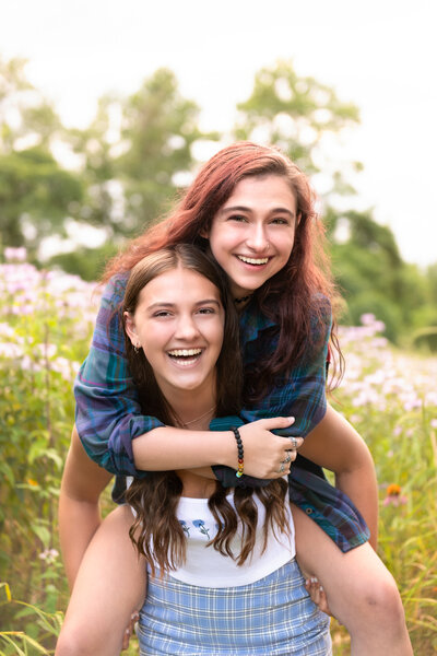 2 sisters laughing piggy back in field of tall grasses