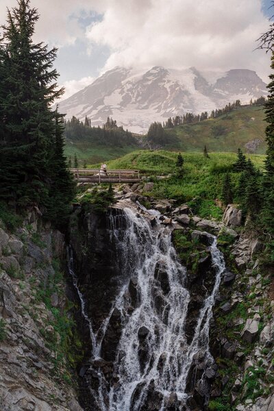 A eloping couple standing on a bridge over Myrtle Falls in Mount Rainier National park as captured by Washington Elopement Photographer Sage Trails.