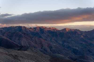 Purple mountains with orange alpenglow on their summits as the sun sets in Death Valley