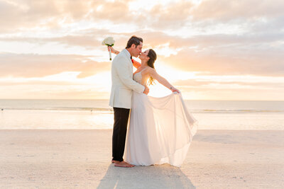 Romantic kiss of bride and groom on the beach at sunset