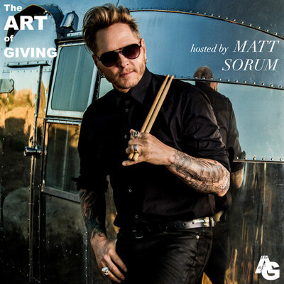 Matt Sorum Instagram promotional image for The Art of Giving standing against silver trailer holding drumsticks as he rests them on his shoulder