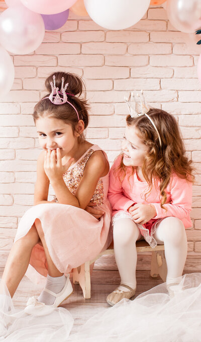 Duo de petites filles assises sur un mini banc et habillées en tenue de princesse rose pour l'organisation d'un anniversaire.