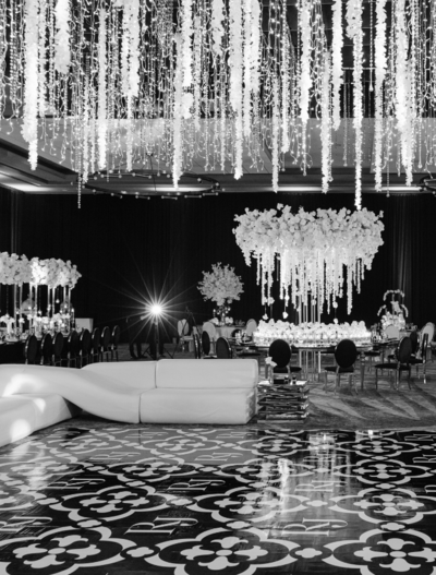 Black and white photo of a wedding reception venue with large floral centerpieces and strands of flowers handing down