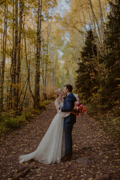 Bride and groom kiss surrounded by yellow aspen trees