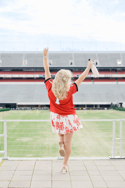 Girl champagne bottle in front of Sanford Stadium in red UGA jersey
