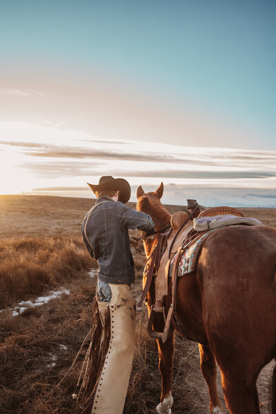 Man/cowboy attending to his horse outside. Picturesque landscape